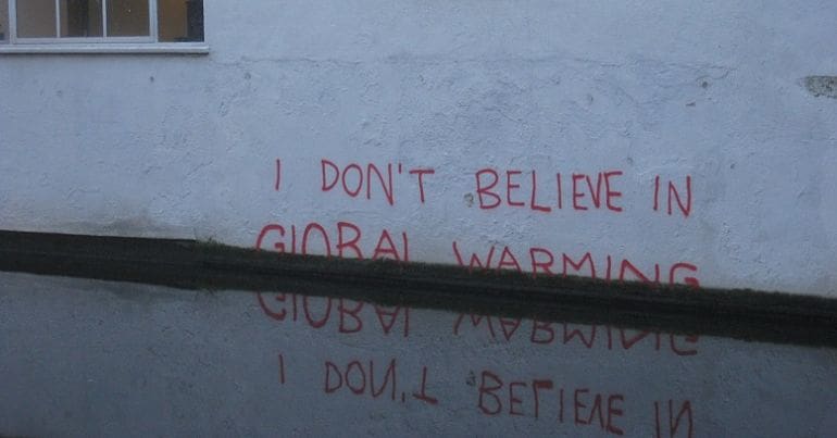 The expression "I don't believe in global warming" ironically slipping dpwn the wall into a puddle