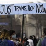 A woman holding a sign saying 'Just Transition Now'