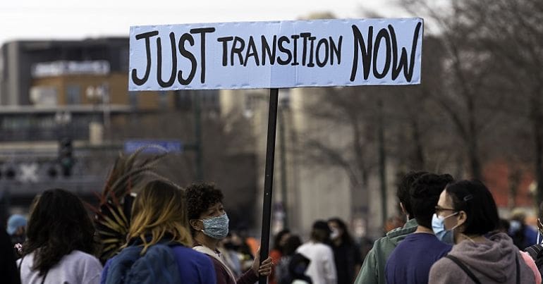 A woman holding a sign saying 'Just Transition Now'