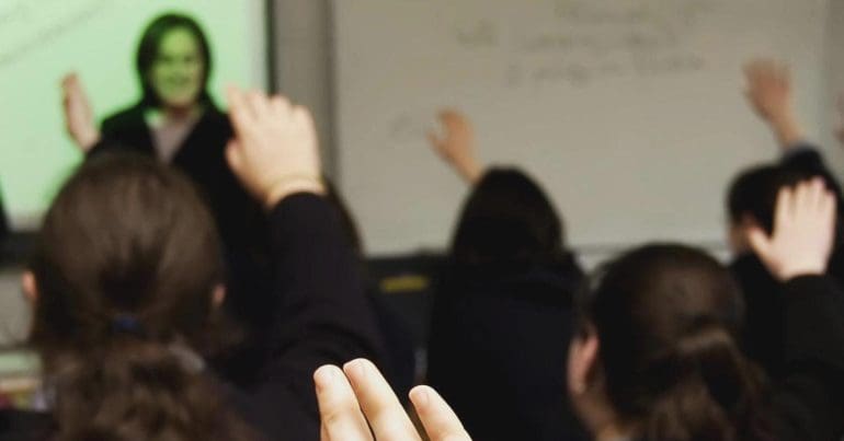 A class room with school children raising their hands