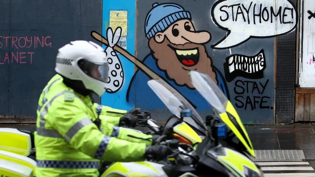 A police officer on a motorbike in front of a mural that advises people 'stay home'