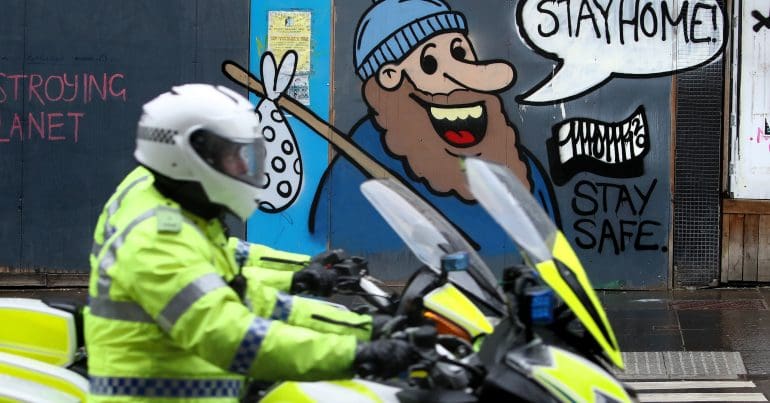 A police officer on a motorbike in front of a mural that advises people 'stay home'
