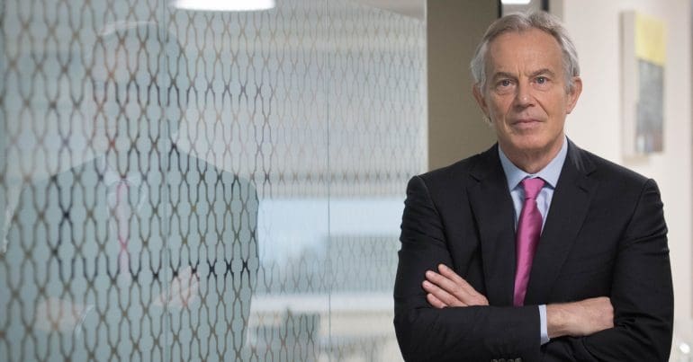 Tony Blair standing to the right with his arms crossed