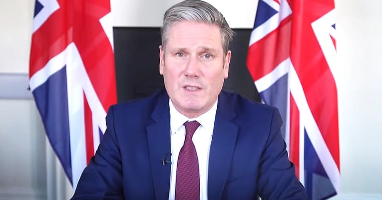 Keir Starmer sitting in front of two Union Jacks