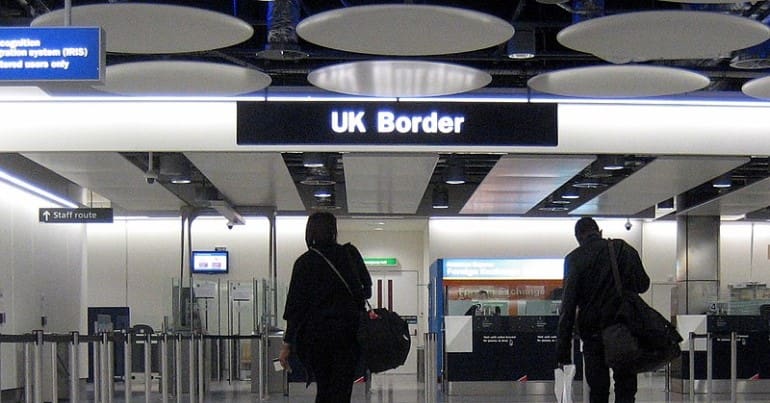 Two people walk away from the camera towards UK border checks at Heathrow airport.