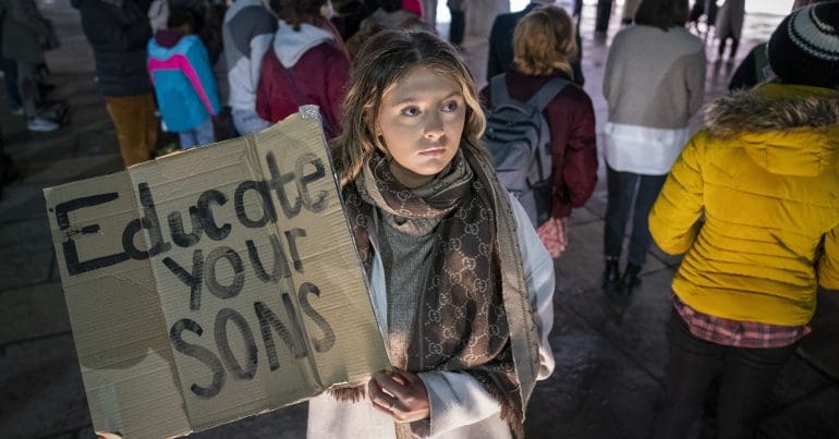 A protester holding a sign which reads "educate your sons"