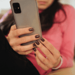 Dark-haired white woman laying back while using her phone