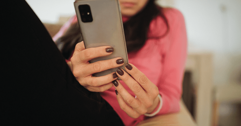 Dark-haired white woman laying back while using her phone