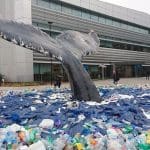 Ocean artwork with whale tail emerging from ocean made up of plastic waste