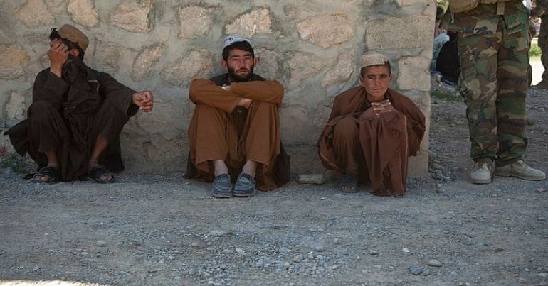 Afghan civilians sit against a wall.