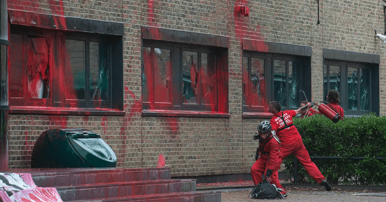Palestin Action activists throwing a fire extinguisher at Elbit Syems offices which are covered in red paint