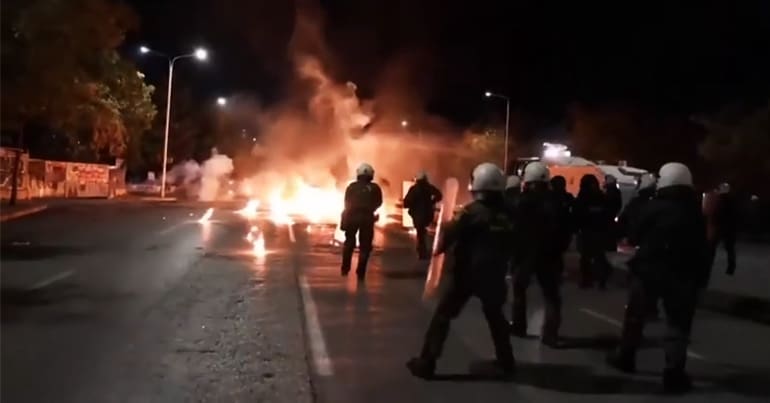 Greek police watch on as a fire burns in the street following the shooting of a Roma teen