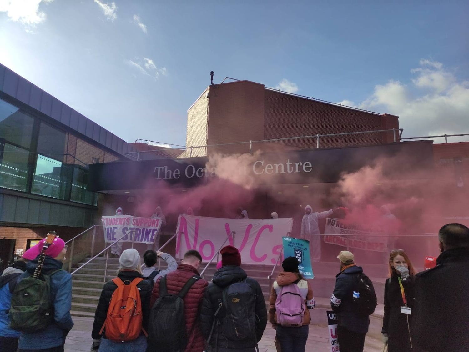 Students occupying universities like this one in Sheffield in support of the UCU strike - a photo of protesters setting of smoke flares and holding banners while people look on 