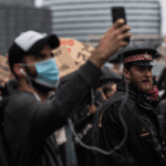 A protestor records on his phone while a police officer looks on during a protest - public order bill going through the House of Lords
