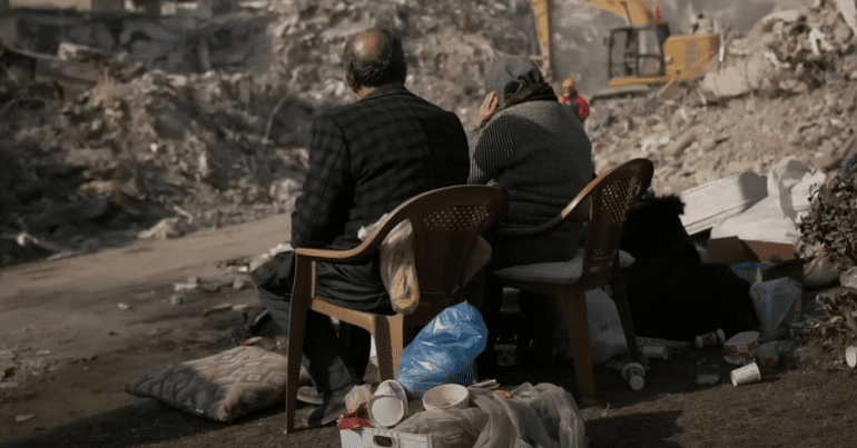 a couple look on at the rubble after an earthquake in Syria