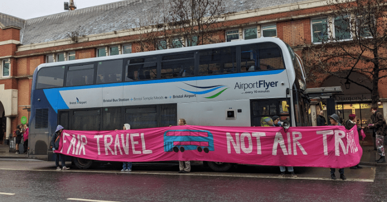 A protest around a bus with a banner that reads 'fair travel, not air travel'. XR Youth Bristol have been targeting buses as part of ongoing action