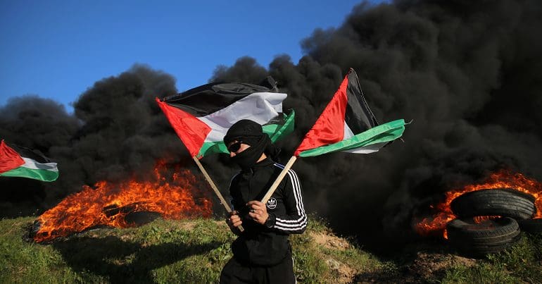 A Palestinian youth waves national flags as others burn tyres, during a protest to denounce the killing of Palestinians by the Israeli army in Nablus near the Israel-Gaza border east of Gaza City, on February 22, 2023.