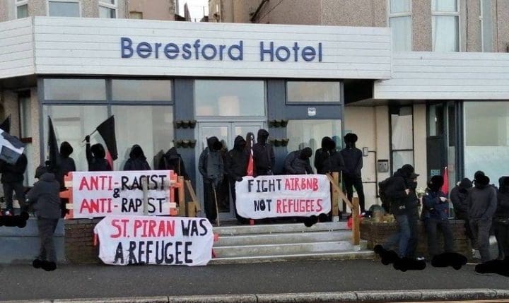 A group of protesters outside the Beresford Hotel. Banners read "anti racist and anti rapist"