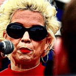 posie parker at a microphone, wearing sunglasses
