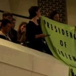 People hold up a banner reading "President of violence" in protest during a speech by Macron in the Netherlands