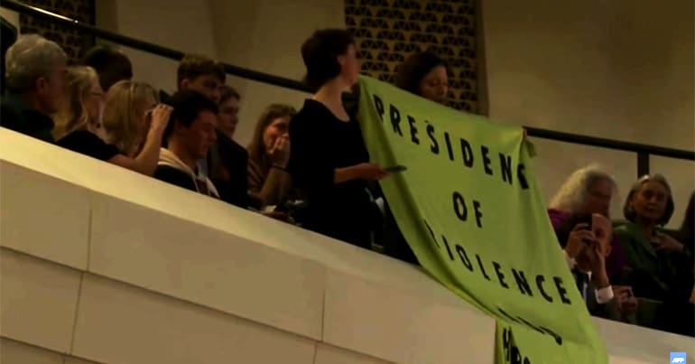 People hold up a banner reading "President of violence" in protest during a speech by Macron in the Netherlands