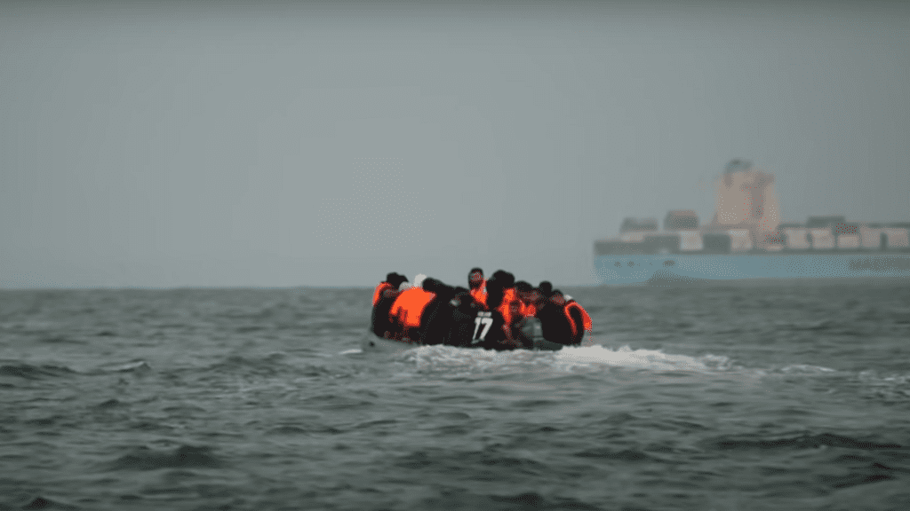 Refugees sit together on a small boat, wearing life vests, illegal migration bill, hostile environment