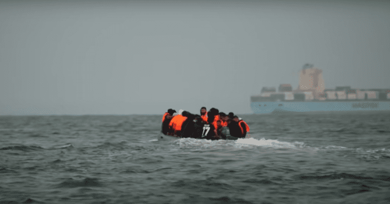 Refugees sit together on a small boat, wearing life vests, illegal migration bill, hostile environment