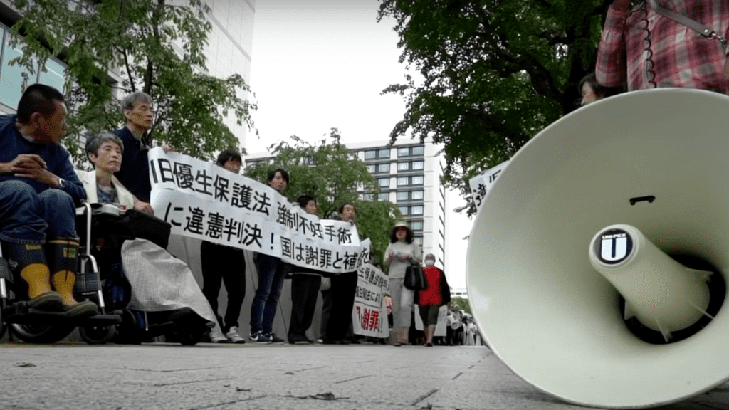 A protest with people standing in a line - the protest is against Japan's forced sterilisation laws and aftermath