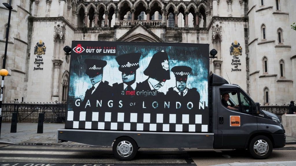 Motor billboard by Police Spies Out Of Lives during the undercover policing inquiry that says "A Met original: Gangs of London" with a cartoon of police officers spycops