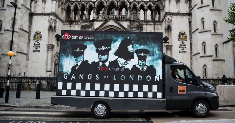 Motor billboard by Police Spies Out Of Lives during the undercover policing inquiry that says "A Met original: Gangs of London" with a cartoon of police officers spycops