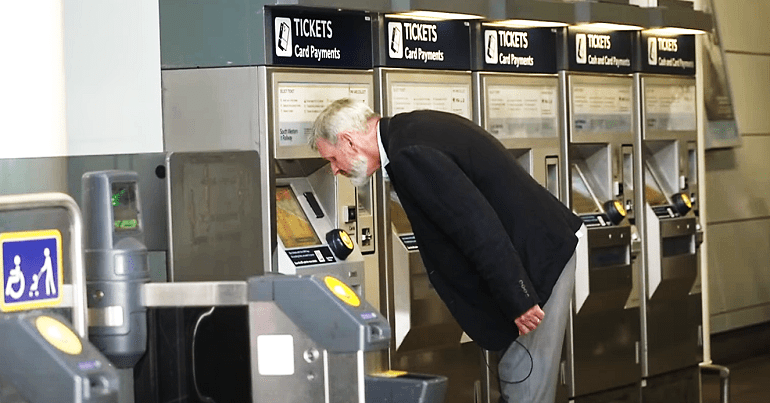 A visually impaired man leaning down to look at a ticket machine ticket office closures DfT