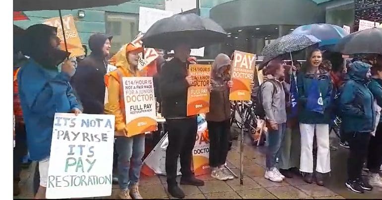 Picket line at Bristol Royal Infirmary hospital with people holding placards demanding 'pay restoration' for junior doctors