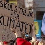 Young climate activists hold up placards in a crowd that state: skolstrejk for klimatet (school strike for climate).