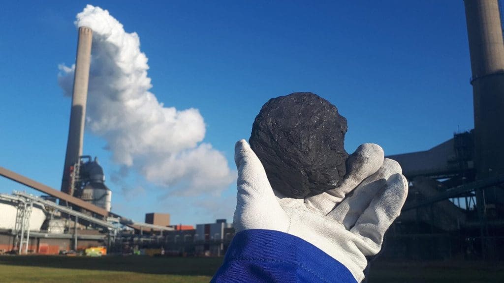 Person holding out a piece of coal in front of a coal-fired power station.