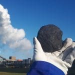 Person holding out a piece of coal in front of a coal-fired power station.