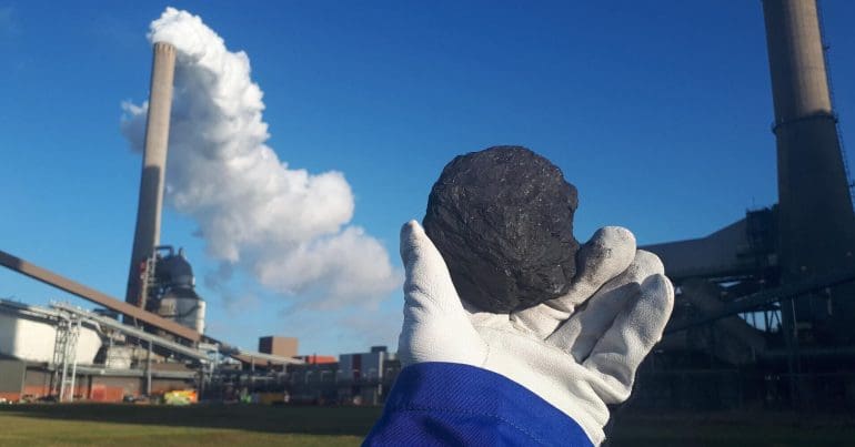 Person holding out a piece of coal in front of a coal-fired power station.