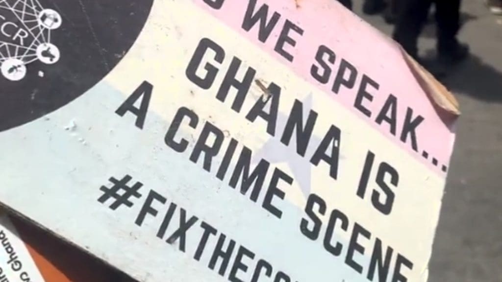 Placard from Ghana protests that says "As we speak... Ghana is a crime scene"