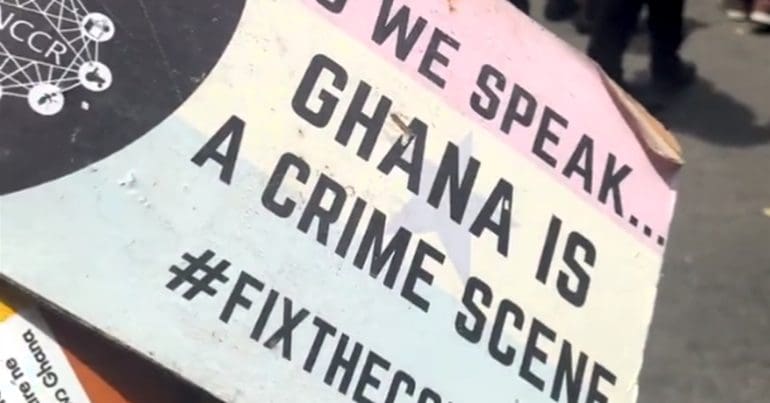 Placard from Ghana protests that says "As we speak... Ghana is a crime scene"