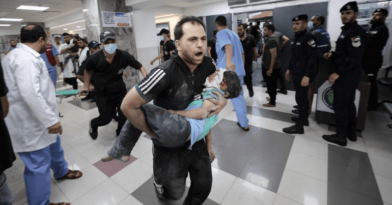 A Palestinian father running through a hospital holding his child while doctors and soldiers watch