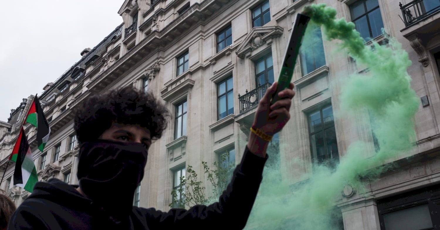 Masked up pro-Palestine marcher in London holds a green smoke flare