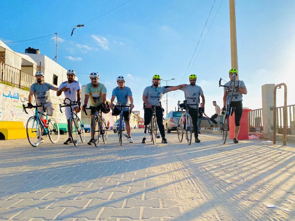 The Gaza Sunbirds stationary and lined up looking at the camera. It is a sunny day with a clear blue sky. The team are near the beach. 