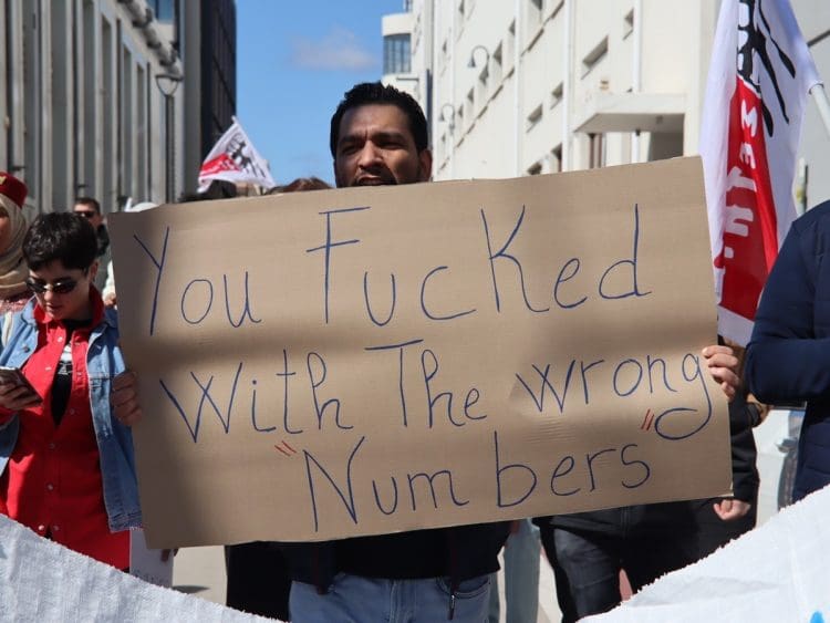A greek call centre worker holding a placard that says you fucked with the wrong numbers