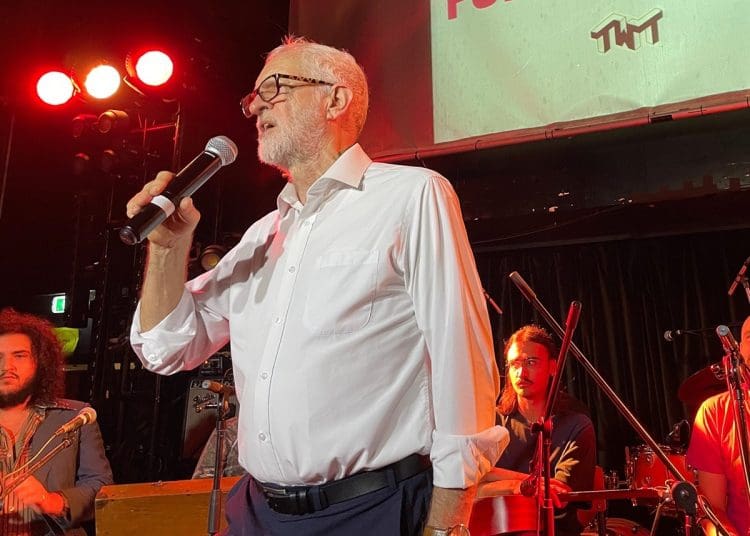 Jeremy Corbyn holding a mic in front of a band