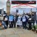 Long Covid Awareness Day campaigners standing in front of Big Ben holding placards with a Guardian headline superimposed and crossed out