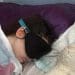 Millie in hospital wearing a face and ear coverings wrapped in a blanket severe ME
