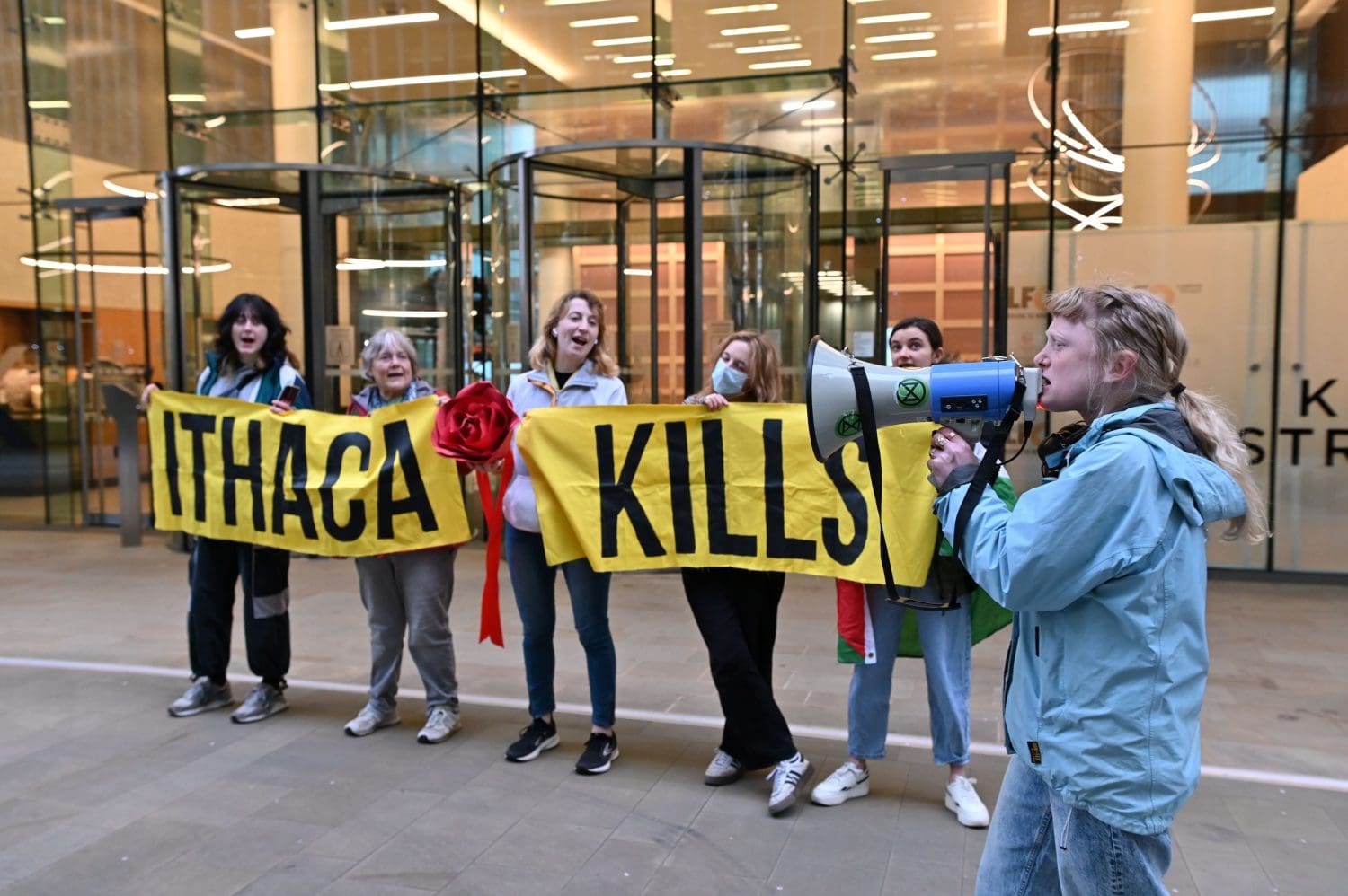 Fossil Free London protesters hold banners declaring "Ithaca Kills" while an activist marches with a megaphone in front.