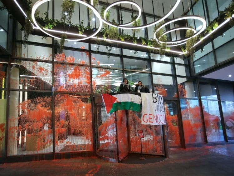 Palestine Action BNY Mellon action glass covered in red paint with two activists sitting