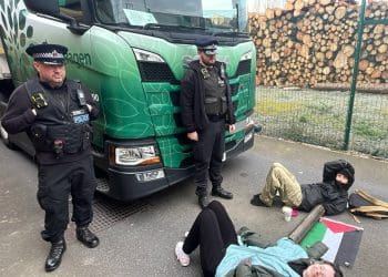 Palestine Action activists laying locked on on the floor with cops watching
