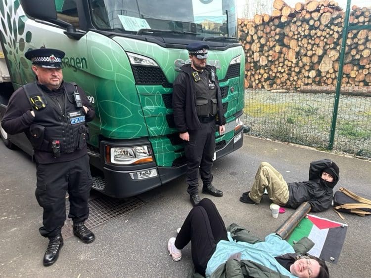 Palestine Action activists laying locked on on the floor with cops watching