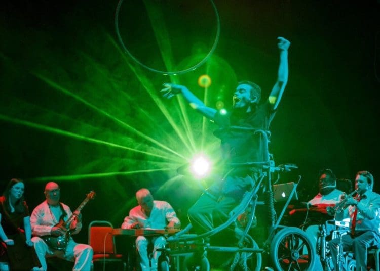 British Paraorchestra disabled musicians with a disabled dancer against a green light